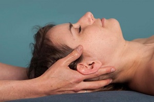 A patient's head rests on the hands of a therapist during a Craniosacral Therapy session.